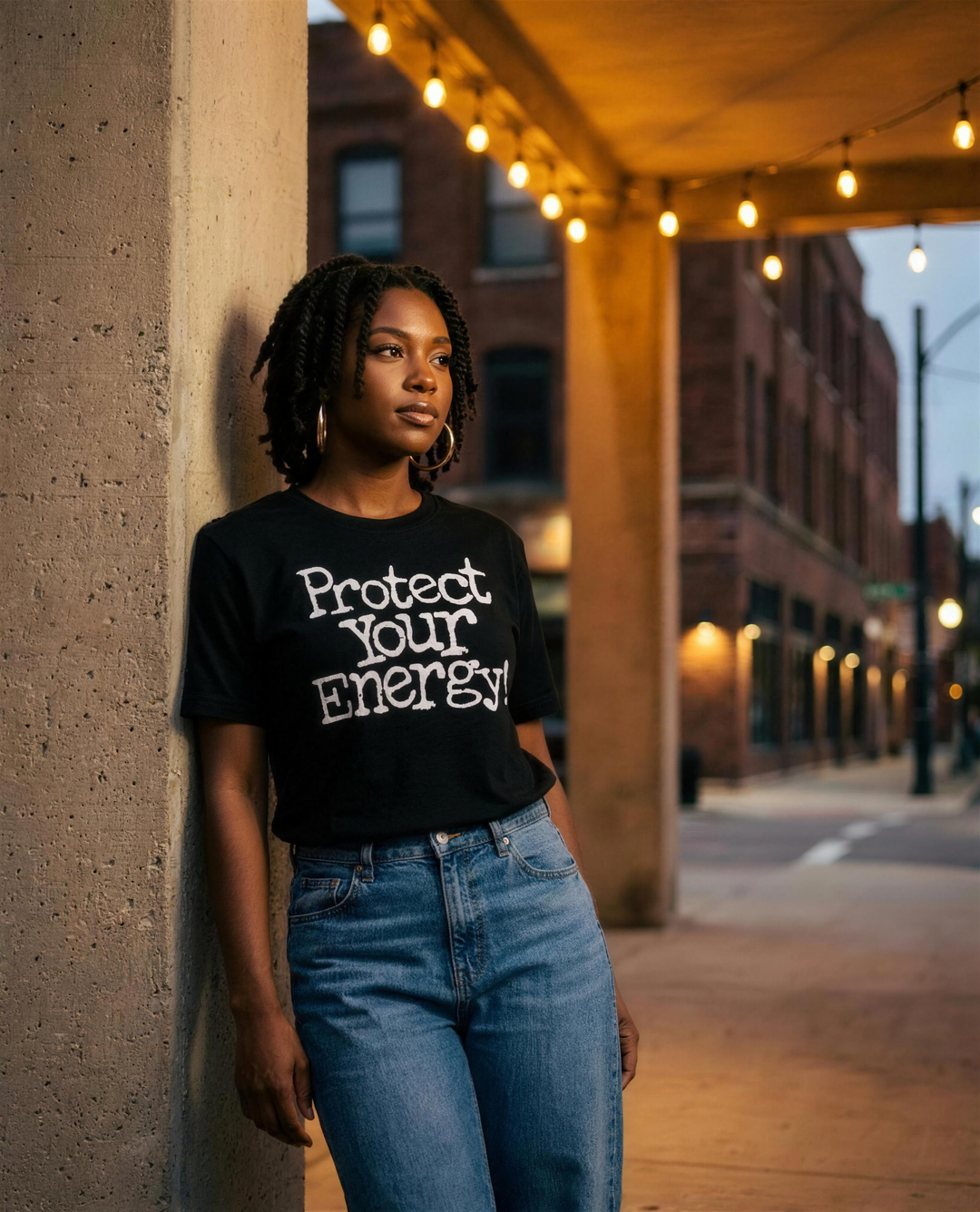 Black woman wearing the Retro Black Protect Your Energy unisex t-shirt under warm evening lights in Detroit