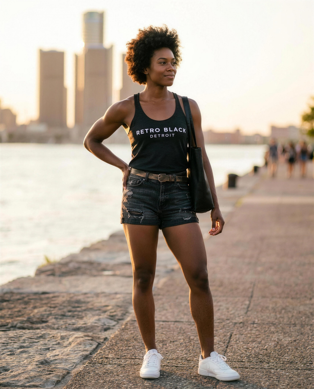 Black woman wearing the Retro Black Detroit racerback tank on the Detroit riverfront at golden hour